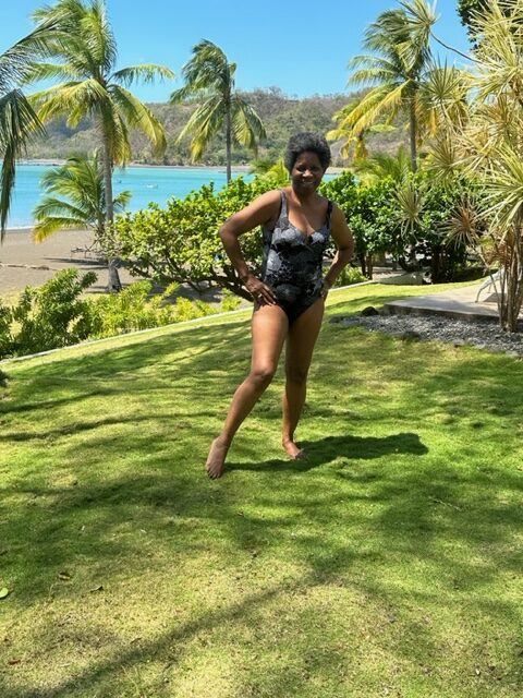 A woman in a black bikini posing in front of the ocean.