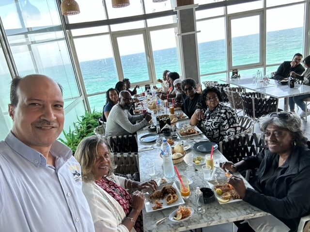 A group of people sitting at a table near the ocean.