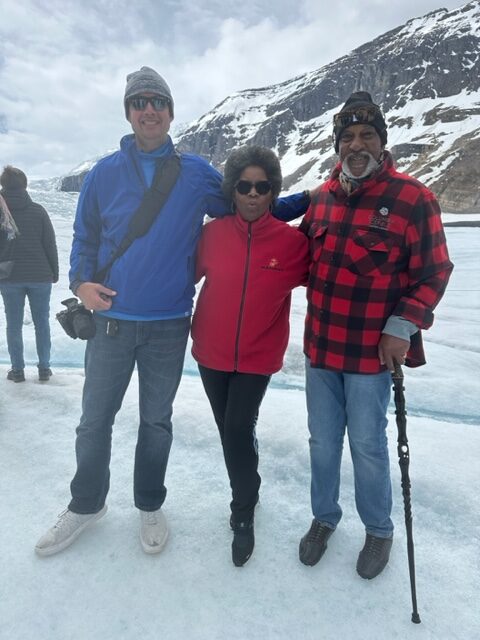 Three people standing in front of a glacier with mountains in the background.