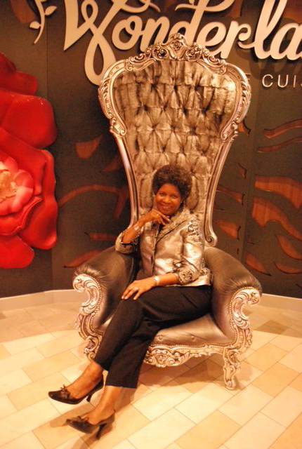 A woman sitting in a silver chair in front of a wonderland cafe.