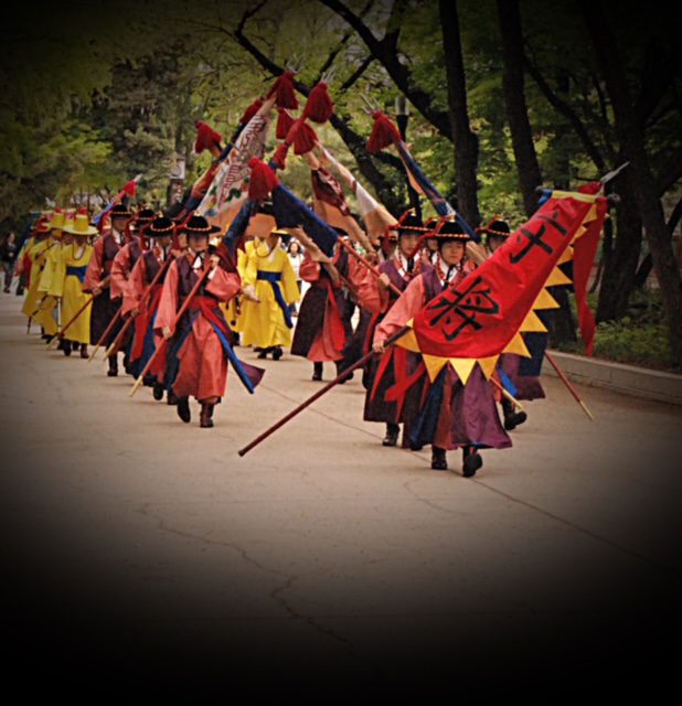 A group of people dressed in traditional korean costumes marching down a street.