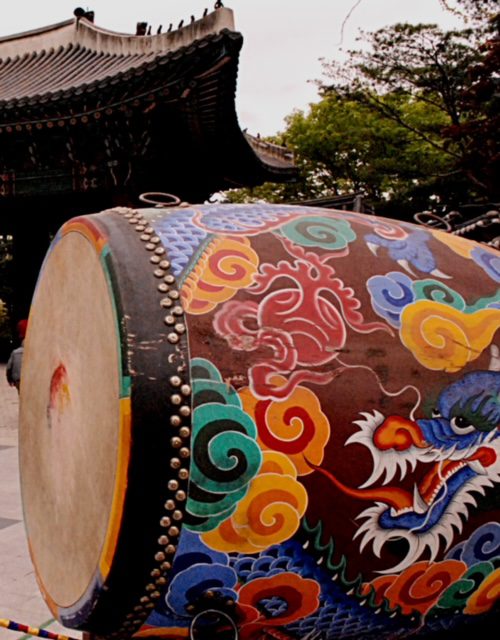 An asian drum decorated with dragons in front of a building.