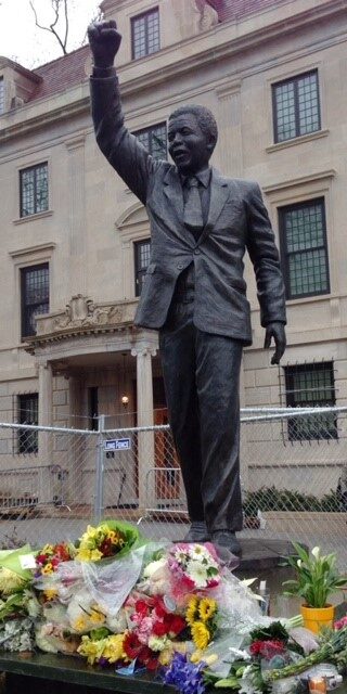 A statue of Nelson Mandela with a building in the back.